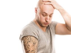 Grimacing man holding head and looking at large tattoo on his arm